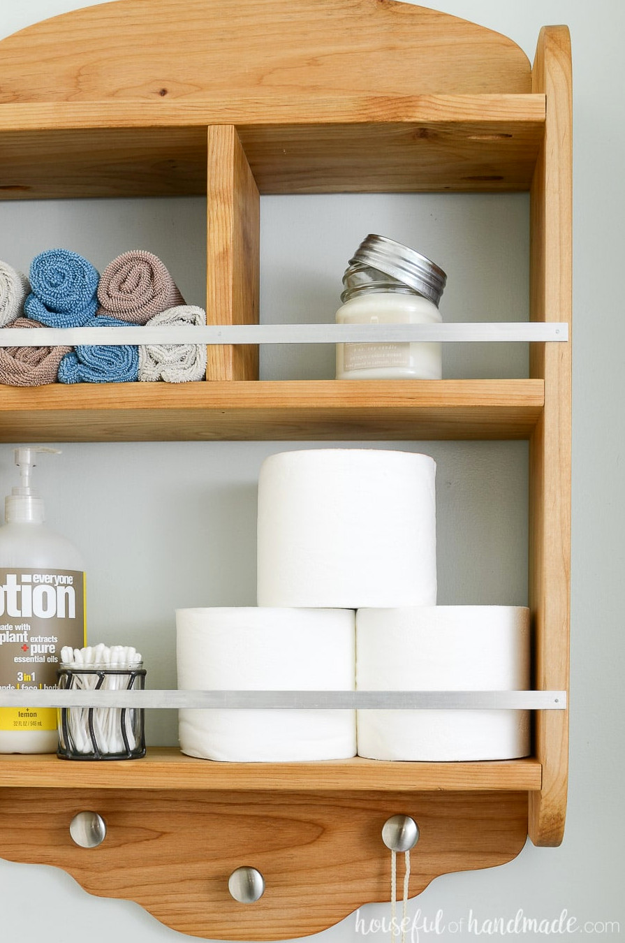 Close-up of the bathroom storage shelves. Metal rails secure items on the shelves, while knobs underneath provide hanging space.