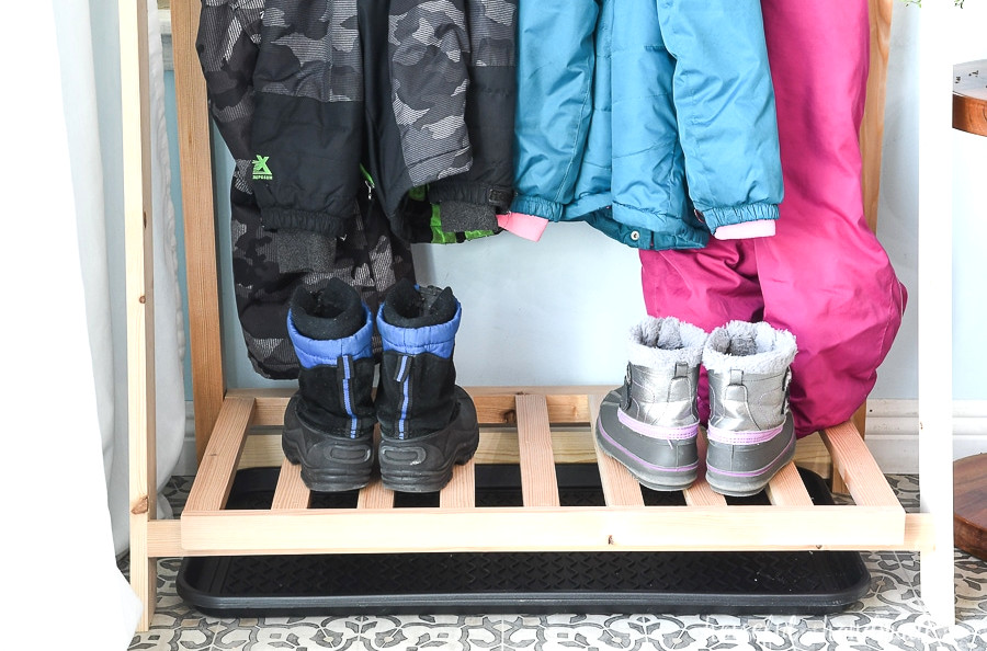 Close-up of the bottom shelf on the fold-down storage shelves with snow boots and a drip tray underneath for collecting melted snow. 