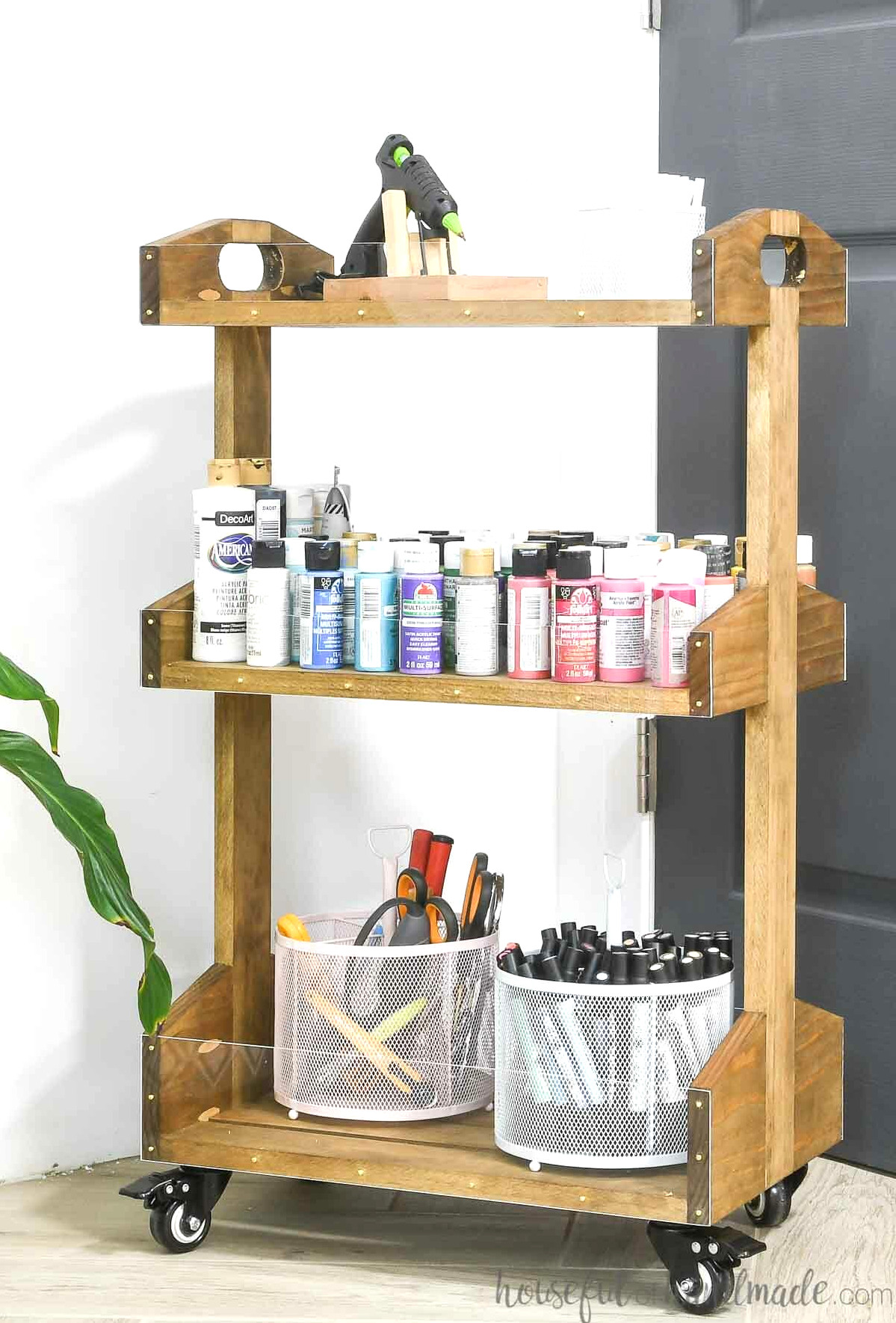 Close view of the simple-to-make wooden rolling cart holding craft paint and a glue gun.