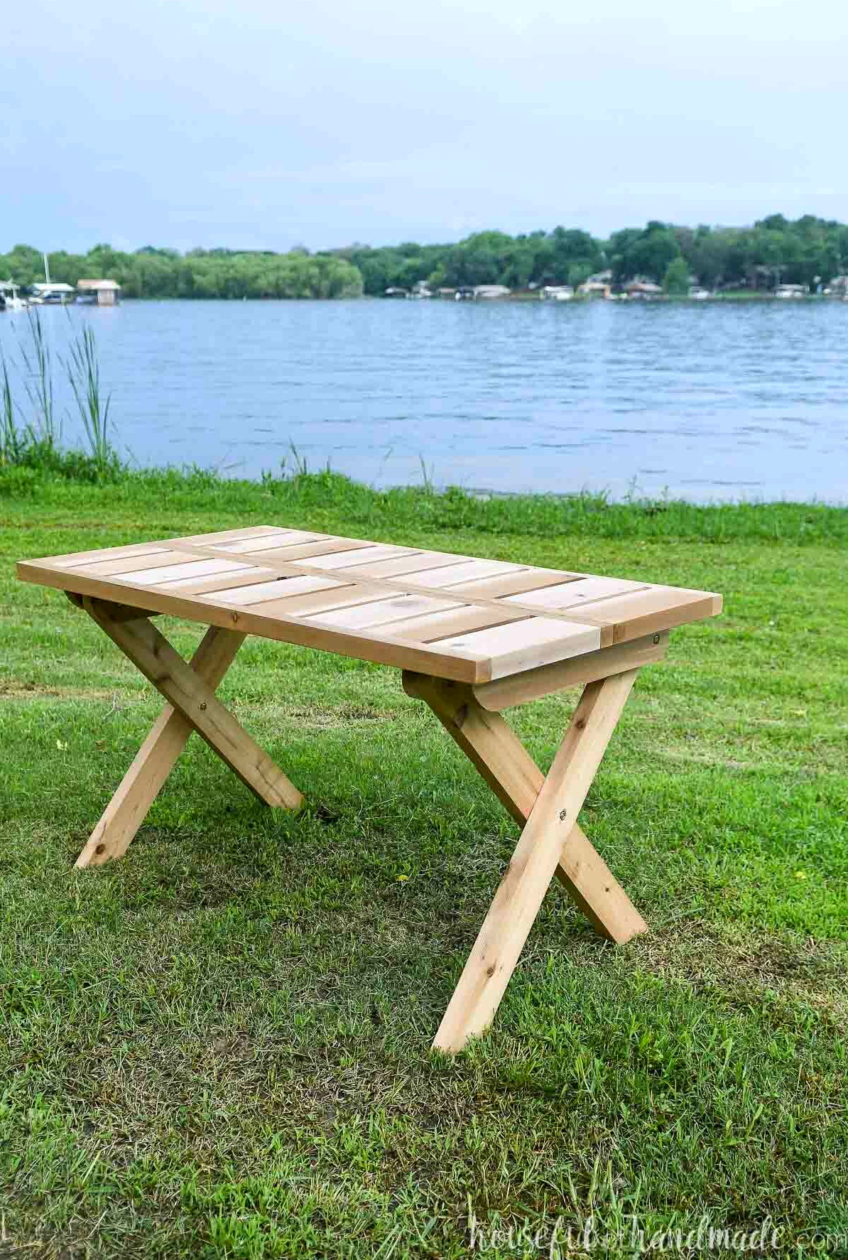 Cedar folding picnic table assembled on the grass beside a lake. 