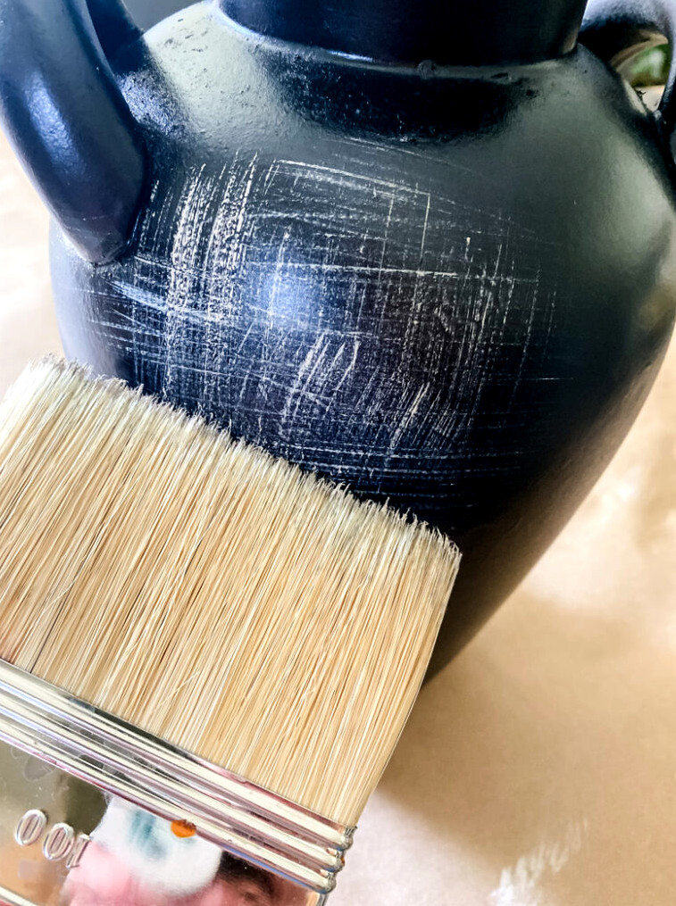 applying cream-colored paint details to a vase