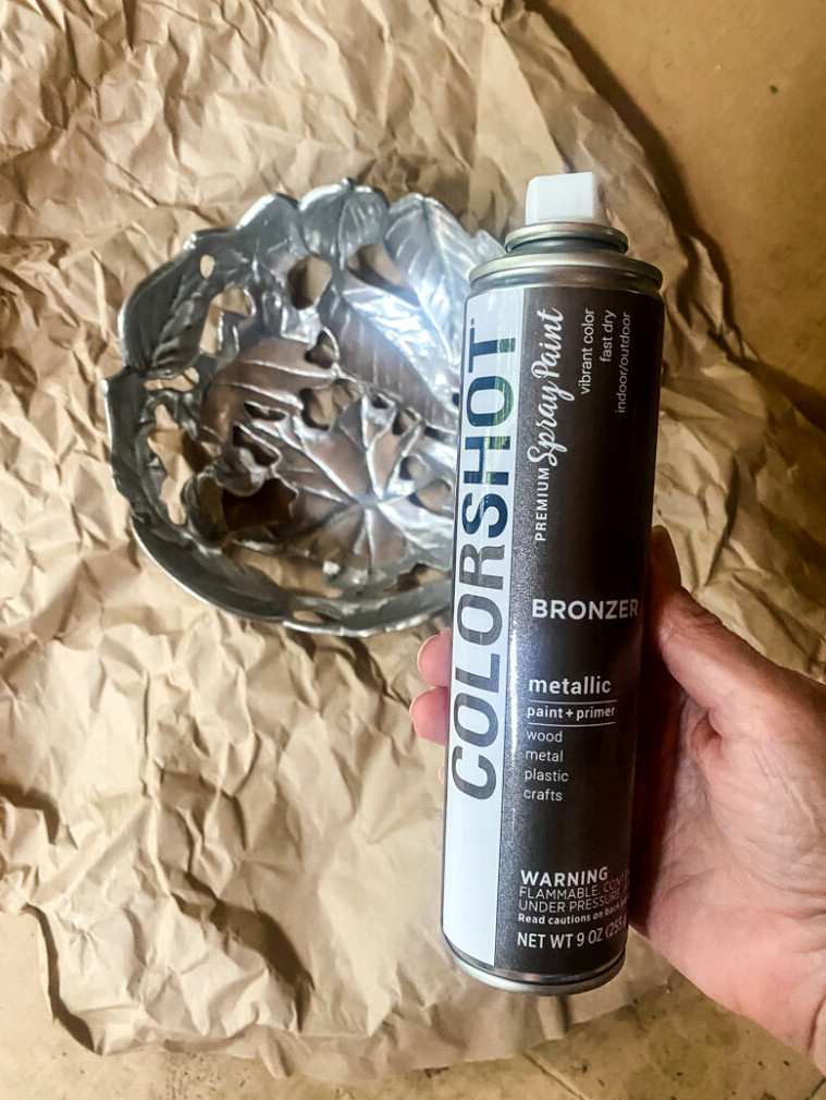 holding a can of colorshot paint getting ready to paint a silver metal dish