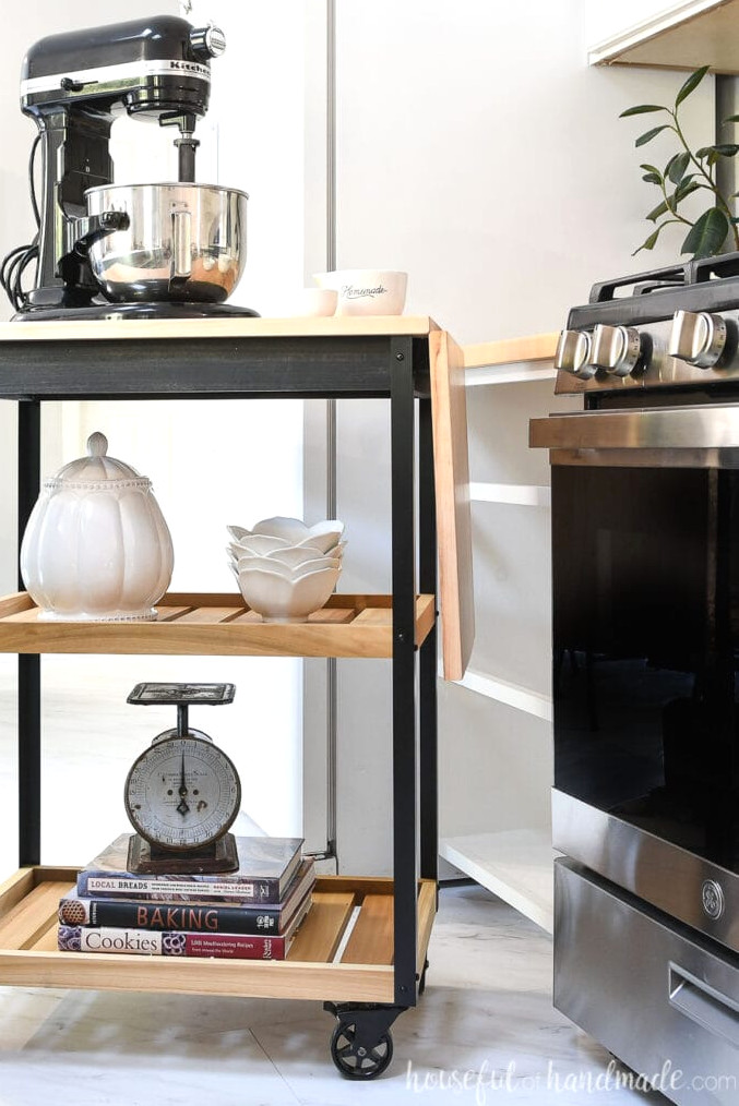 Natural wood and black rolling kitchen cart with metal corners and black wheels in a kitchen. 