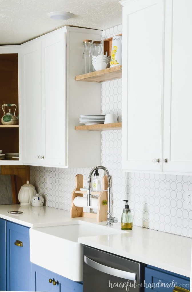 Detailed view of the white wall cabinets in a two-tone kitchen. A farmhouse sink sits below open shelving.