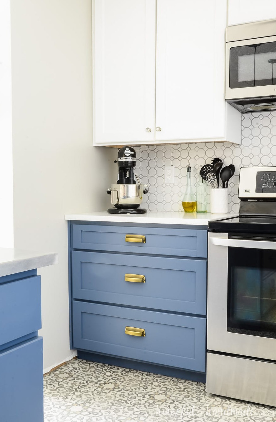 Blue painted drawer base cabinet with 3 drawers next to the stove with white upper cabinets, tile backsplash and countertop.