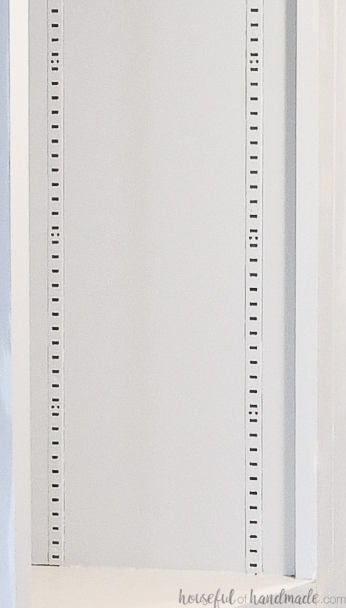 Close-up of shelf standards fitted into a groove along the side of a lightly painted bookcase. 