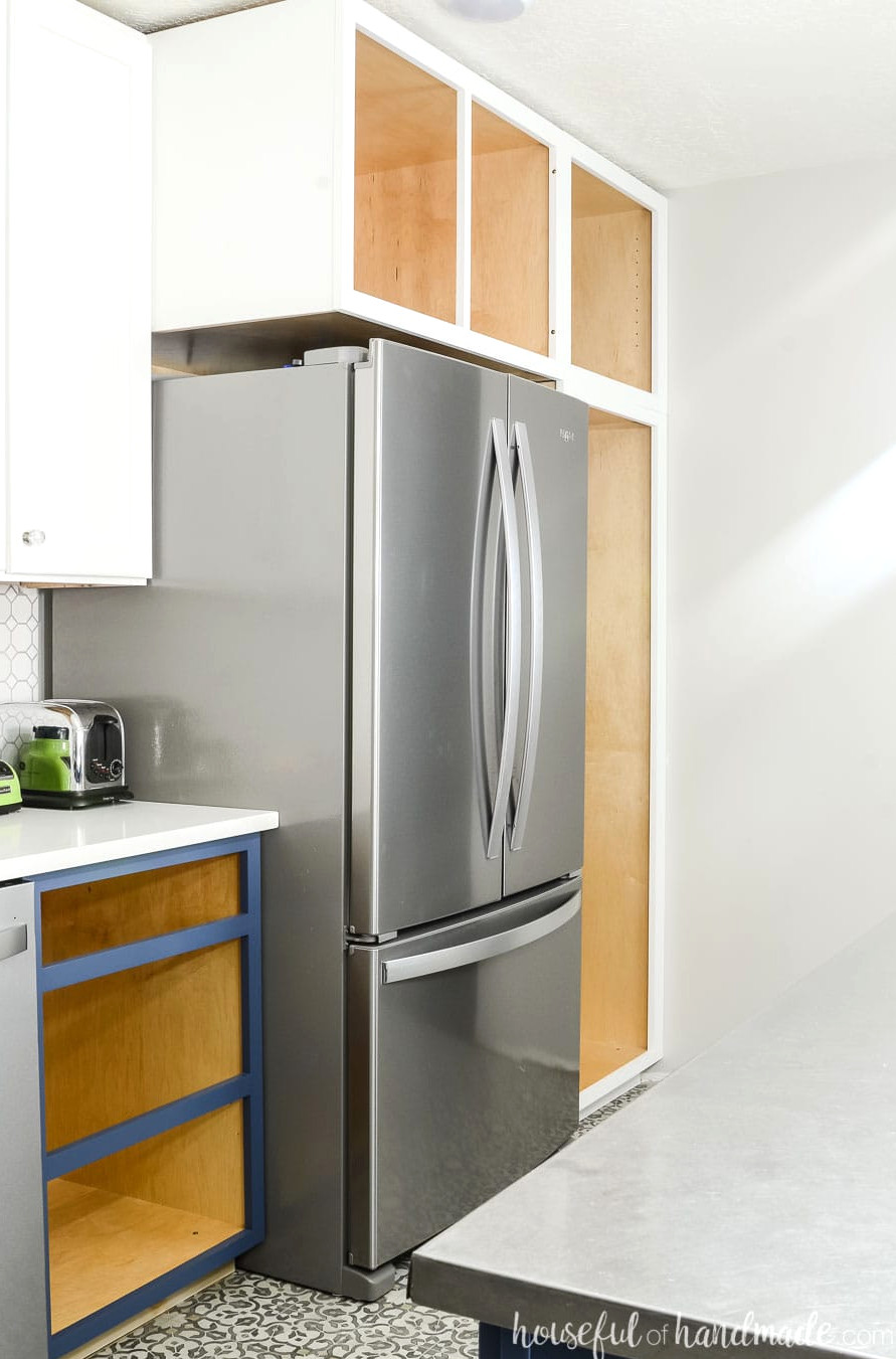 Stainless steel refrigerator surrounded by deep pantry cabinets painted white.