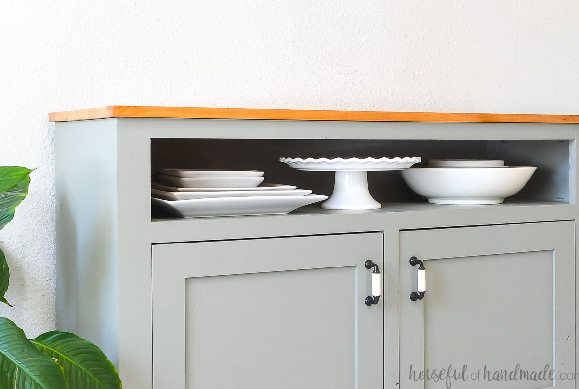 Narrow shelf above the cabinet in a sideboard storing large serving trays, bowls and a cake plate. 