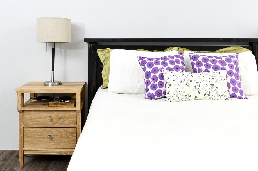 Front view of the DIY queen bed frame, showing a mattress inside with pillows resting against the headboard.