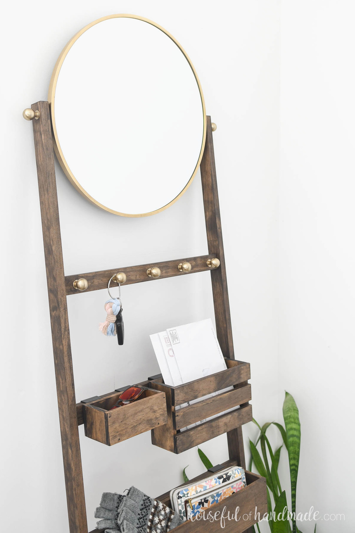 Ladder with round mirror on top and brass knobs for hooks.