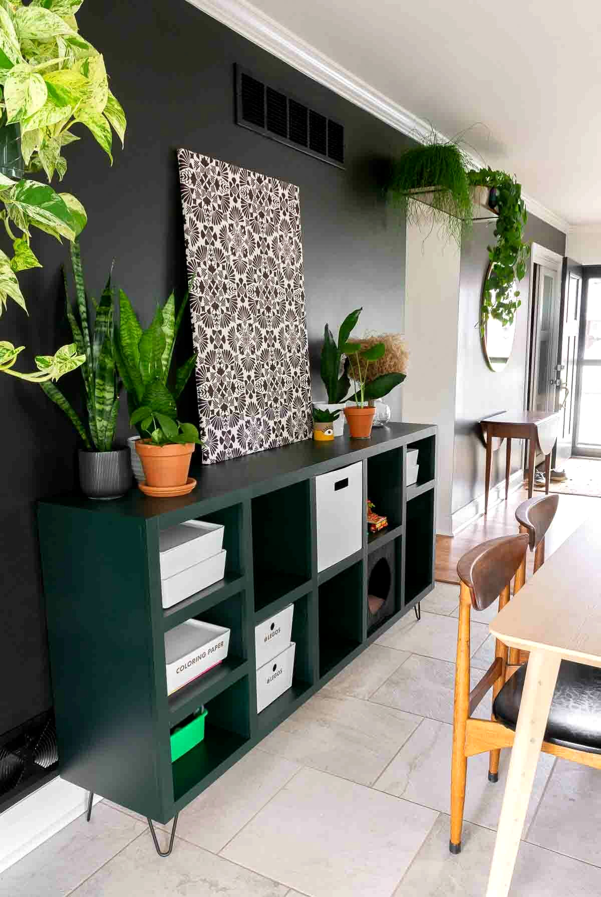 Dark green DIY cube storage shelf with hairpin legs against a black wall in a dining area.