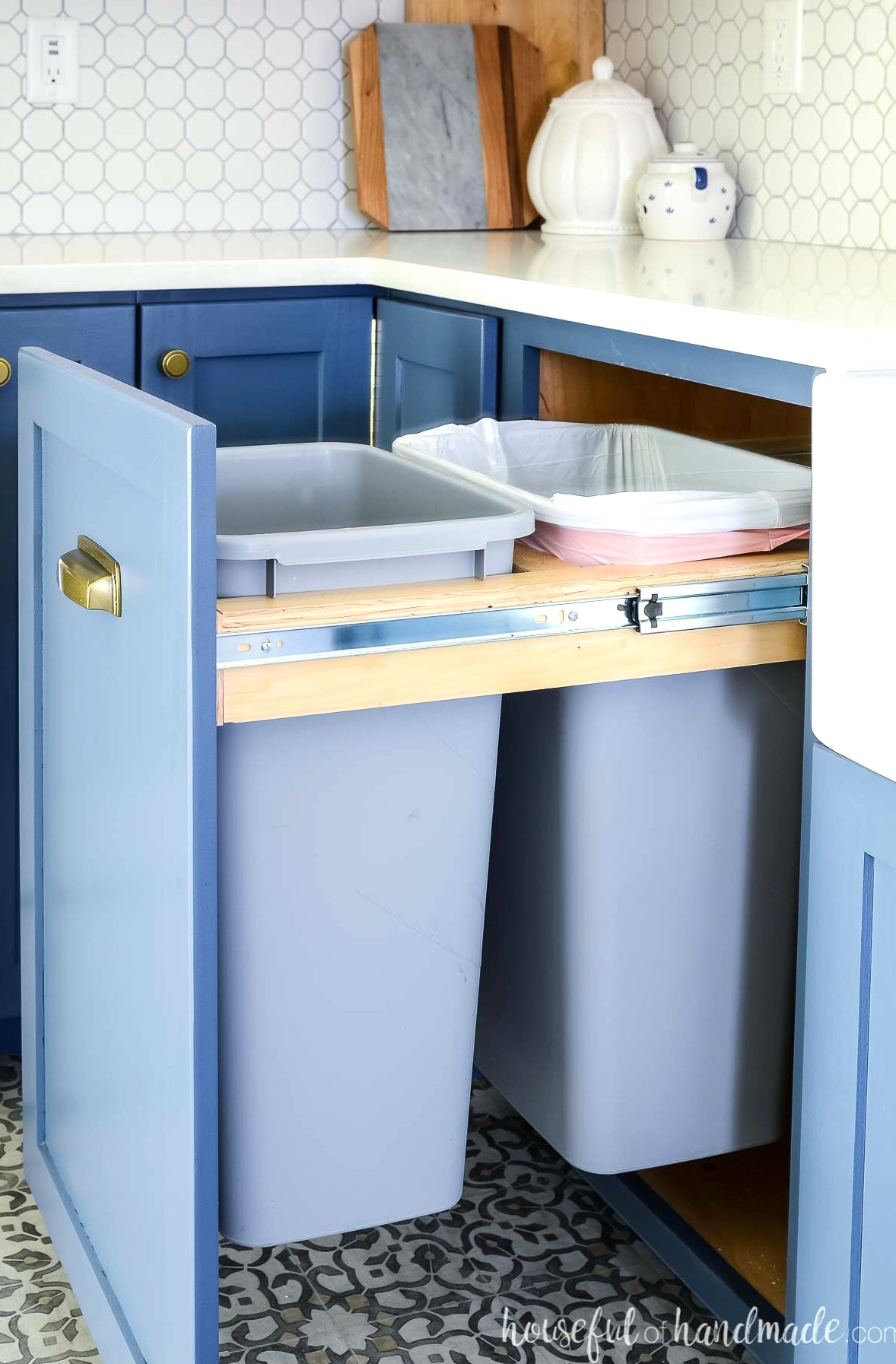 Blue kitchen cabinets with a pull out trash can cabinet holding two full size kitchen garbage cans.