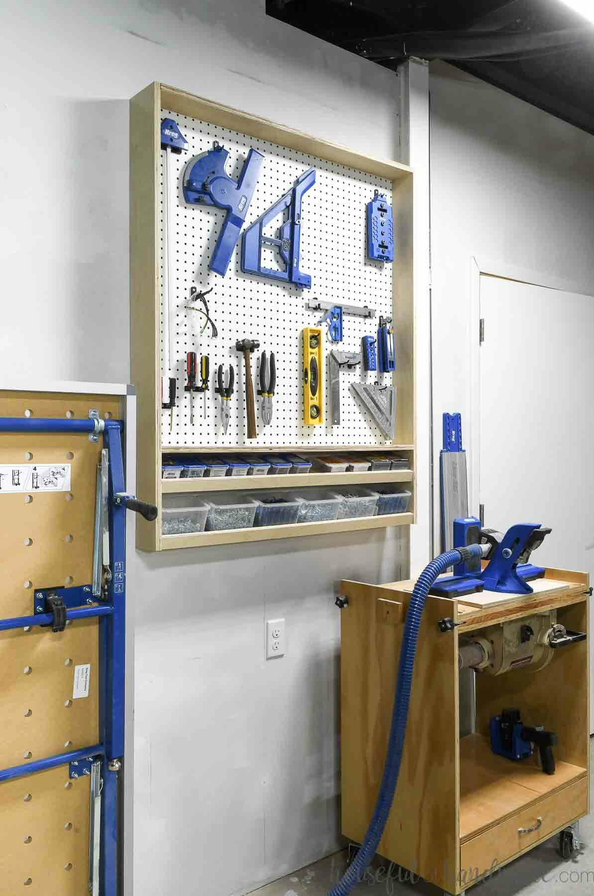 Pegboard storage cabinet mounted on a garage wall with tools displayed on it and larger tools positioned beside it.