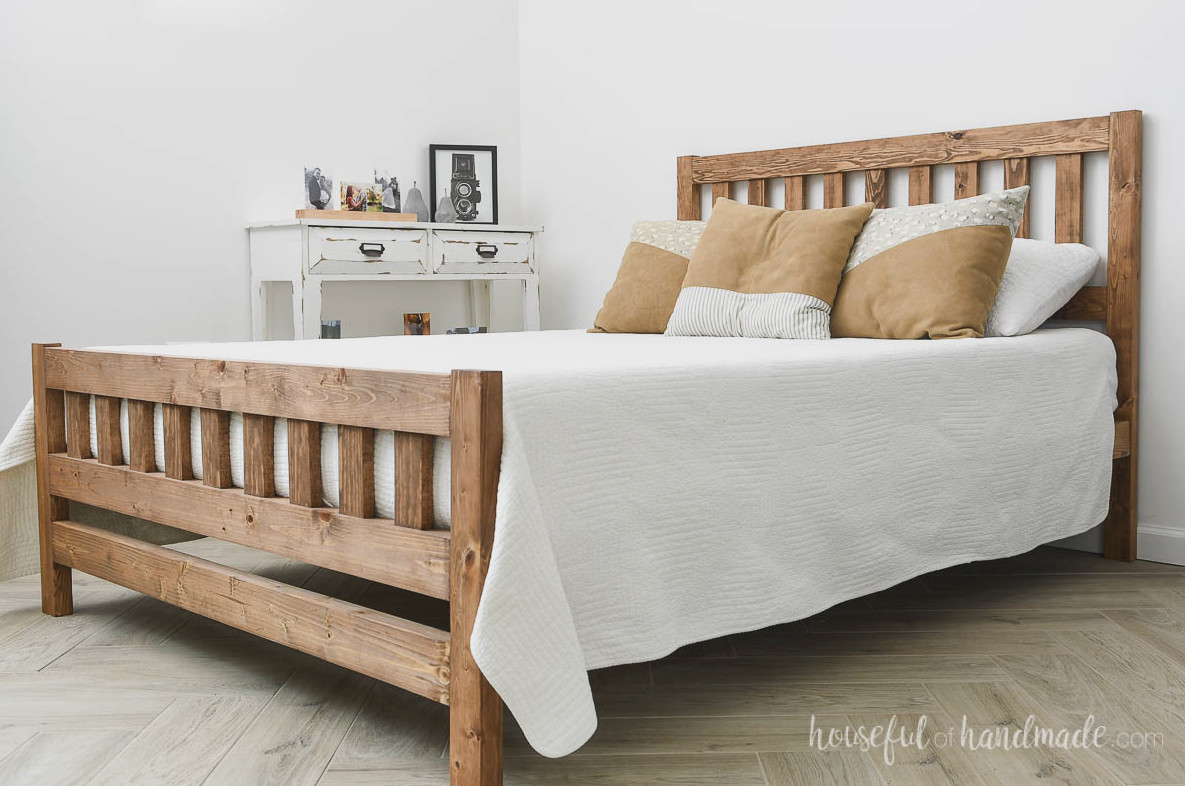 Full sized mission style wood bed with white bedding on a herringbone wood floor. 