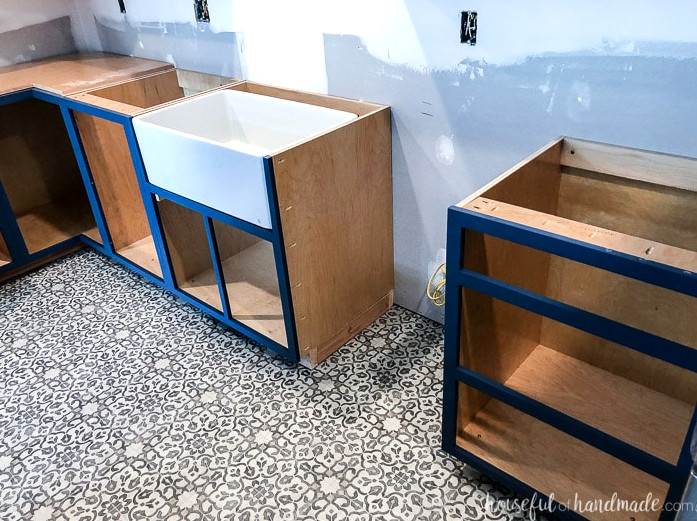 Navy blue face frame DIY base cabinets fitted in a kitchen without doors, including a custom apron front sink base cabinet.