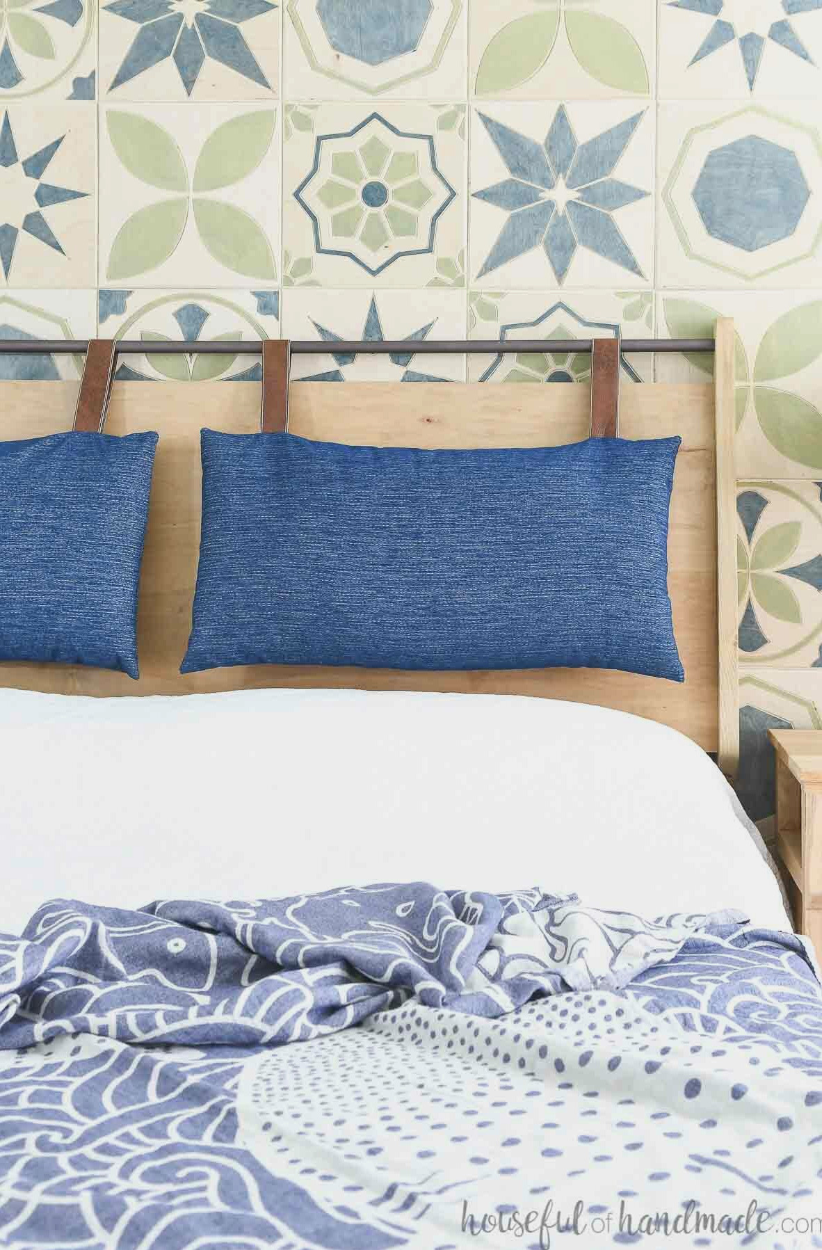 DIY wooden headboard with a metal bar across the top holding two navy and leather headboard cushions.
