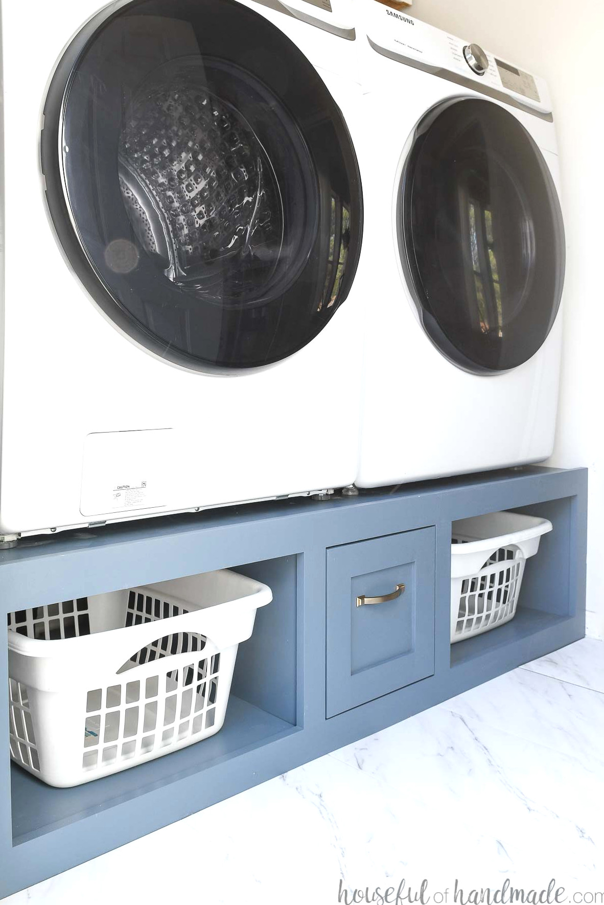 Laundry room with washer and dryer sitting on a blue painted platform with laundry basket shelves and a drawer. 