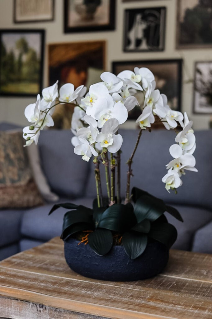 faux orchid arrangemnt on a coffee table with a stylish gallery wall in the background