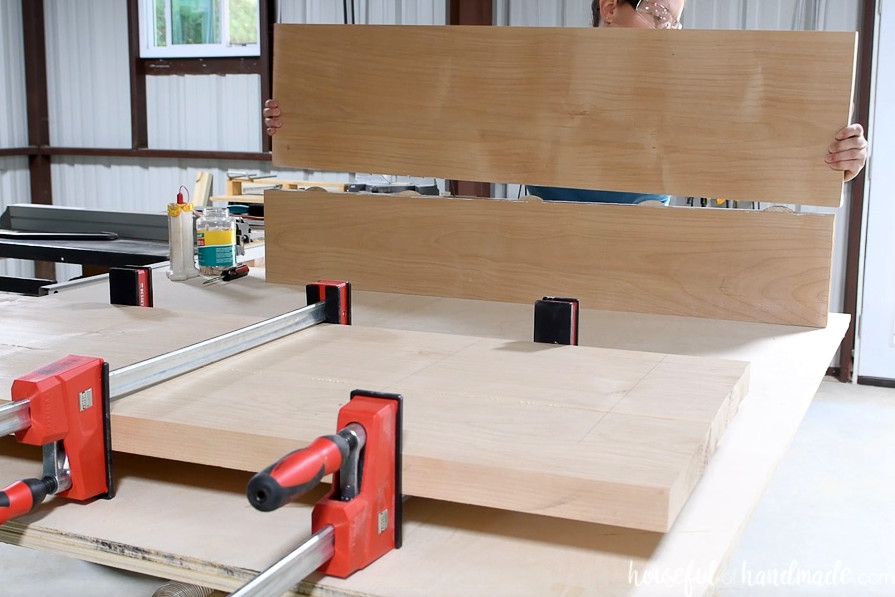 Gluing the second tabletop section in the background while the first section remains clamped in front.