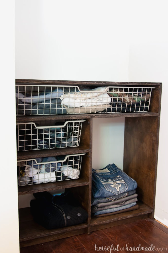 Opposite side of the DIY closet organizer featuring Ikea baskets in the cubbies and folded pants arranged on a shelf.