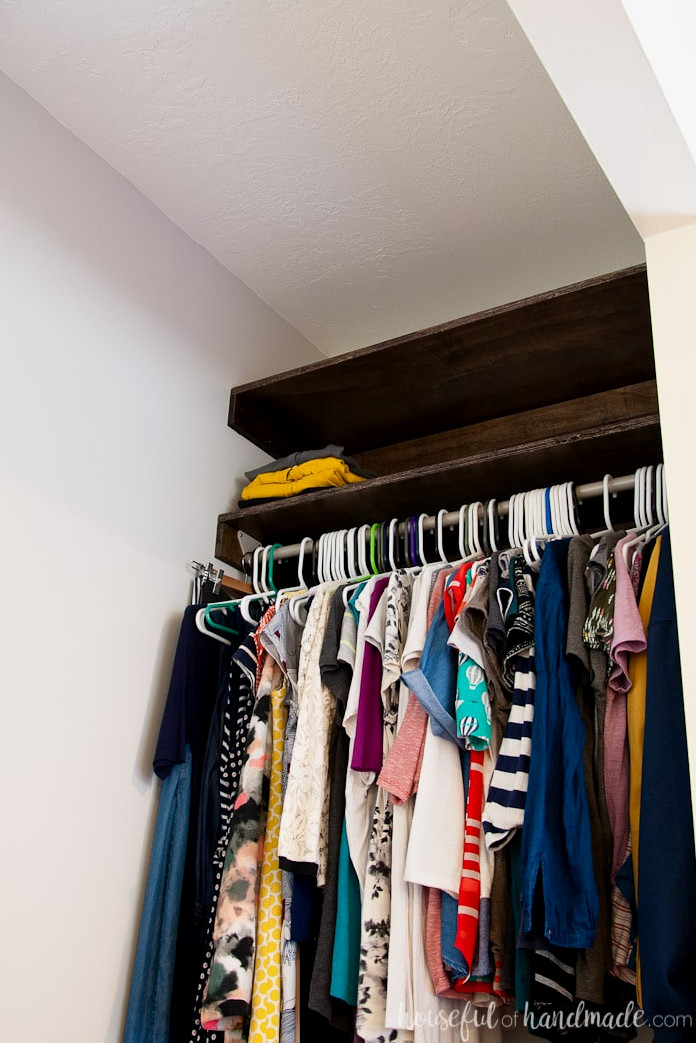 Finished closet featuring a hang bar secured to the shelf supports with clothing hanging from it.