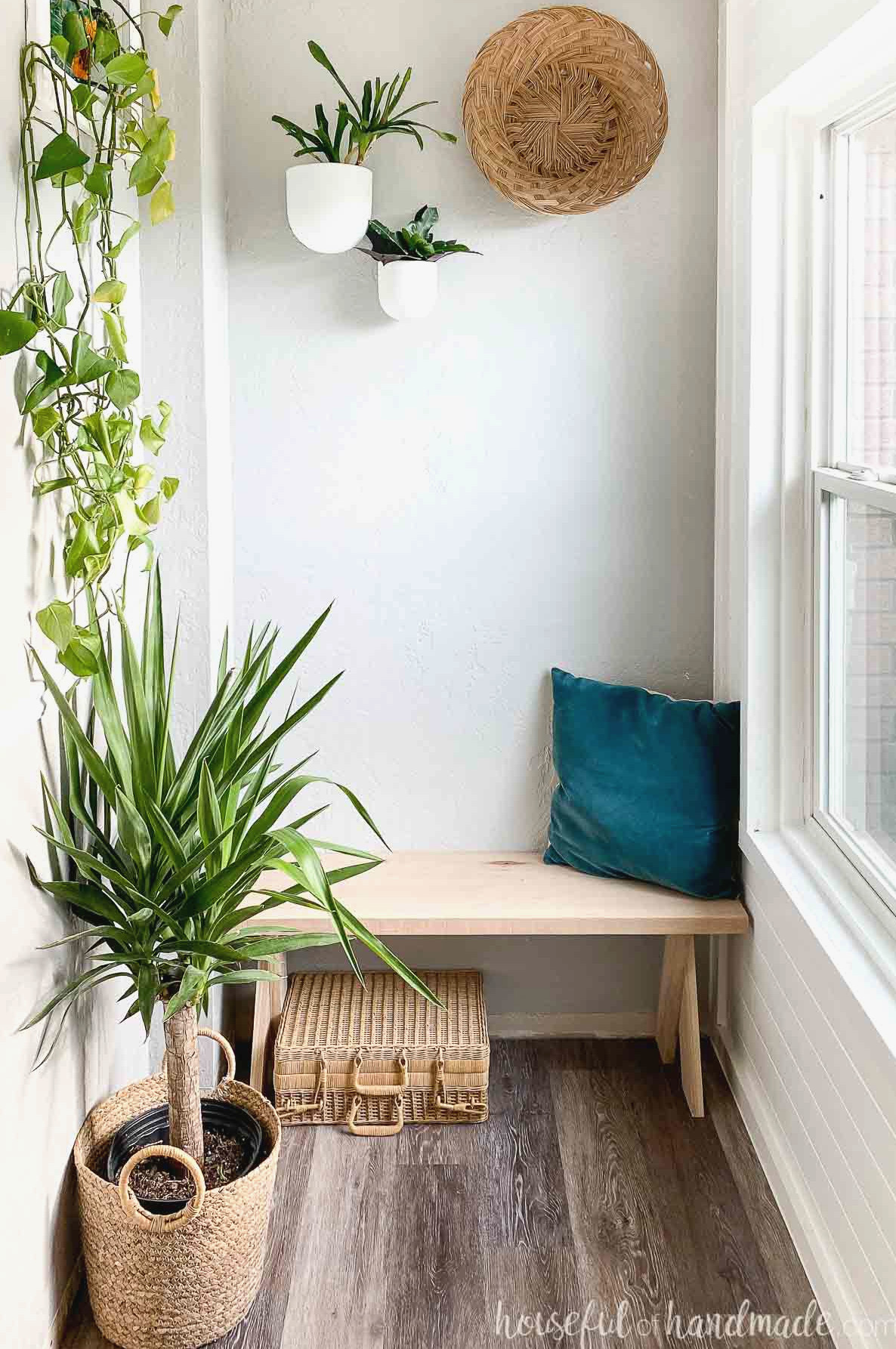 Entry corner filled with houseplants surrounding the DIY bench, with a wicker suitcase placed underneath.
