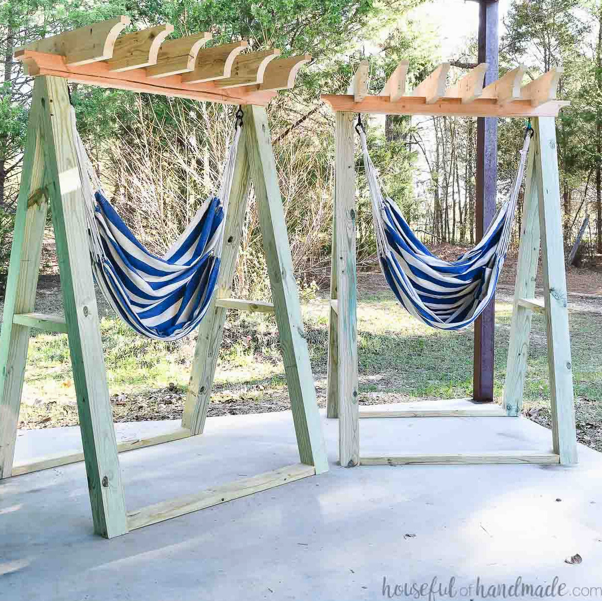 Two hammock chair stands with blue and white striped hammocks hanging from them on a porch.