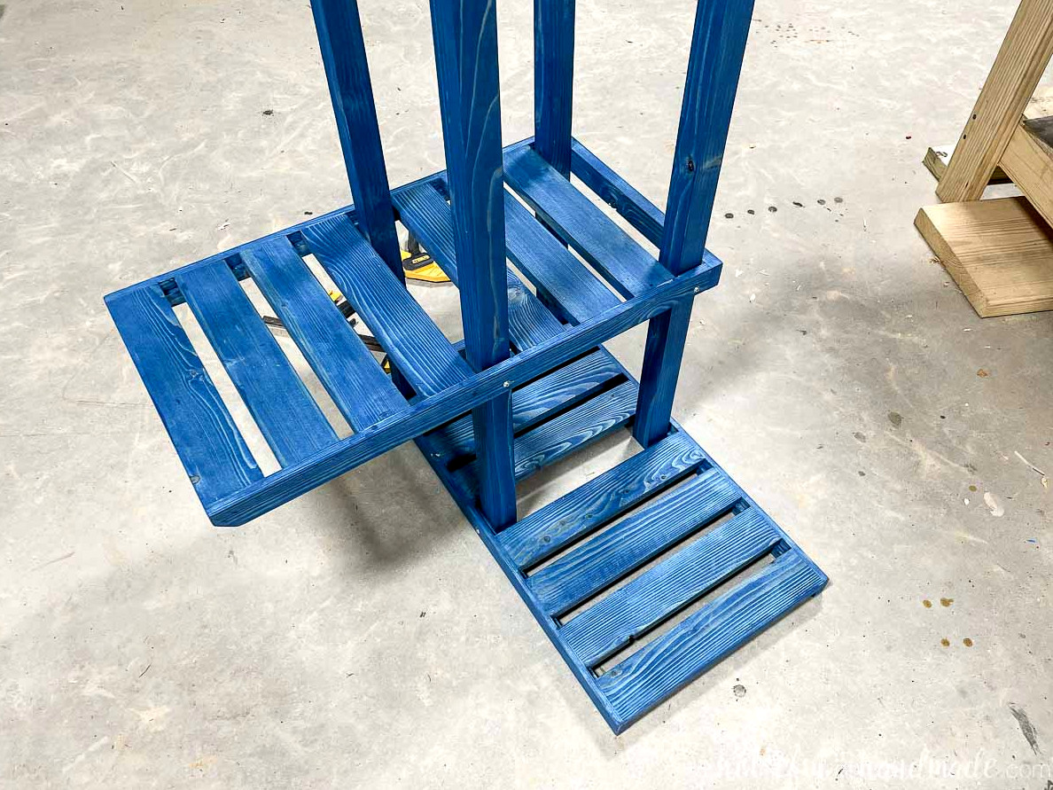 The plant stand being assembled on the floor with two of its 6 shelves secured. 