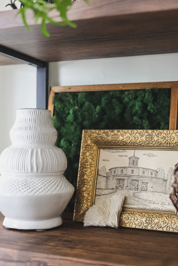bookcase styled with white vase, moss art, and small print