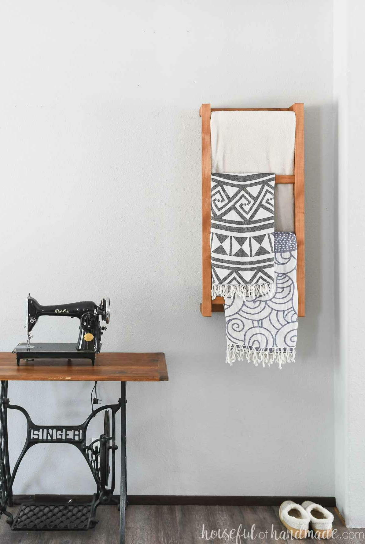 Wall mounted ladder for blankets or towels in a bedroom, with throws hanging from it. 