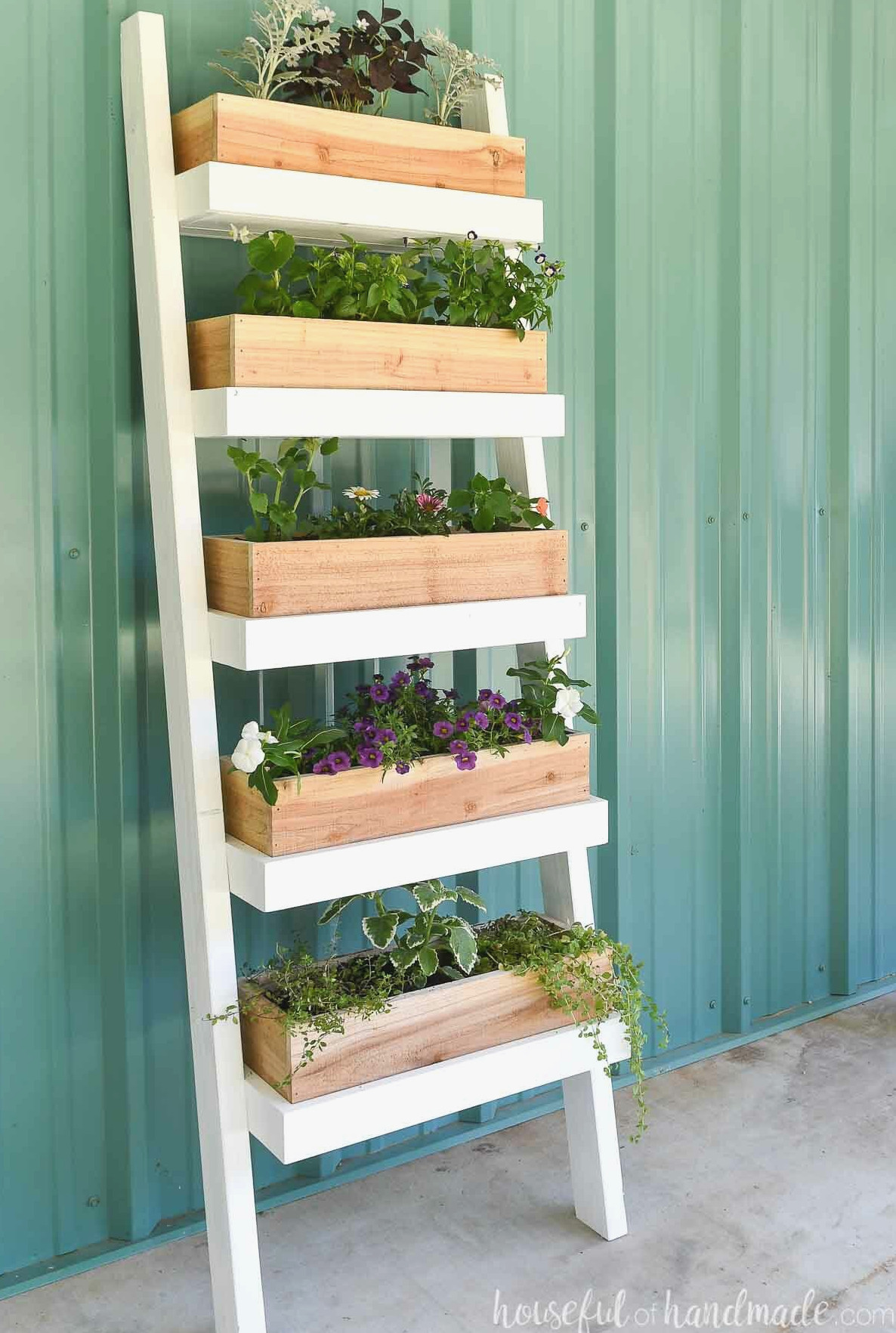 Five tiered ladder planter with plants and herbs planted in it up against a metal building.