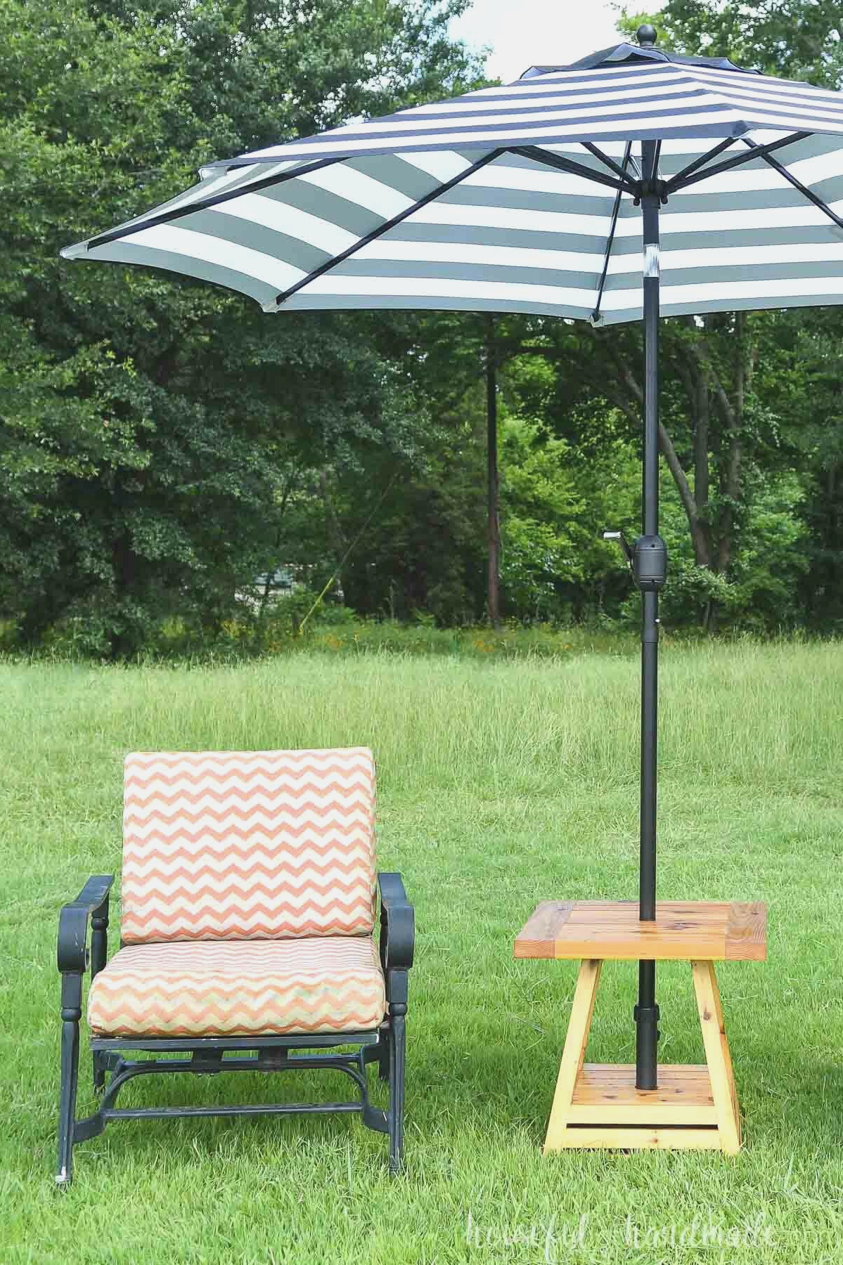An umbrella side table positioned on the grass beside an orange-and-white cushioned chair.