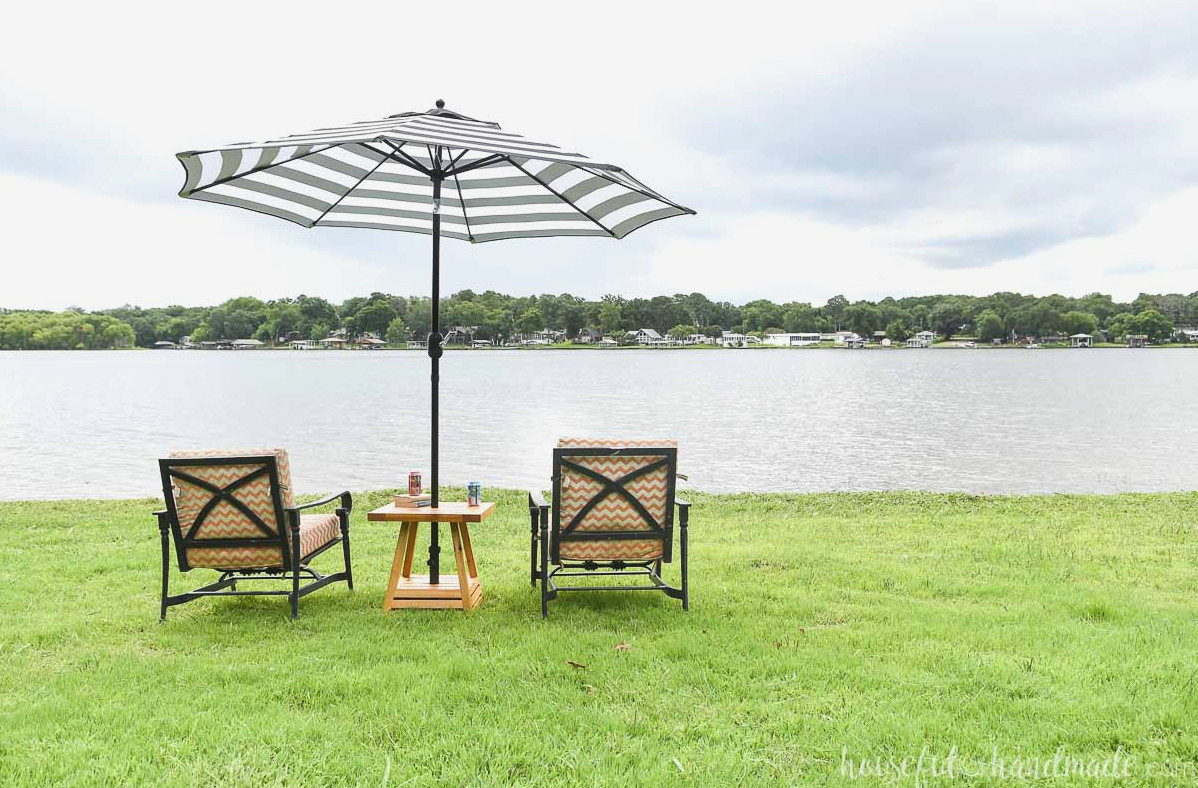 Two patio chairs positioned on either side of an umbrella side table with a lake view beyond.