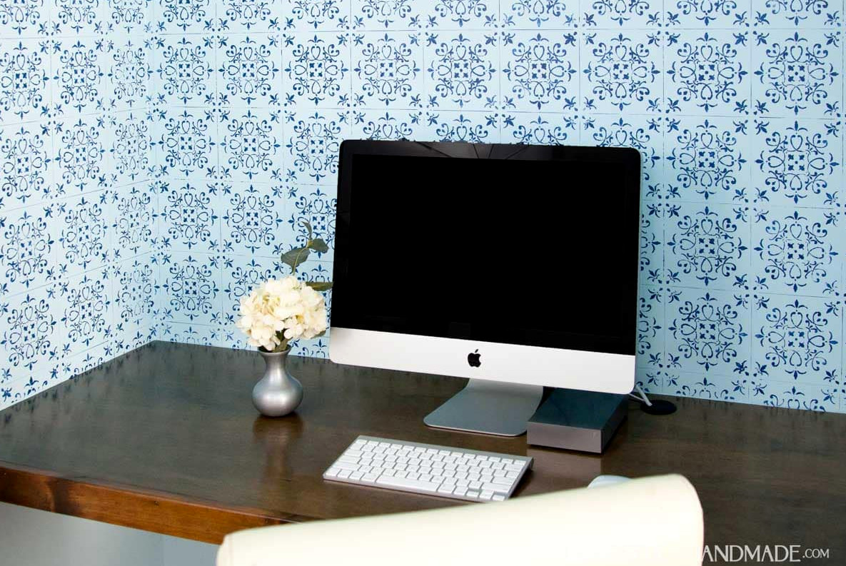 Office in closet shown with finished blue patterned wall paper, wood desk top and computer.
