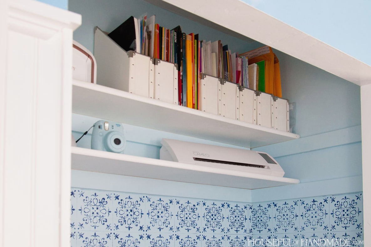 Office closet storage shelves against blue painted walls decorated with a stencil.
