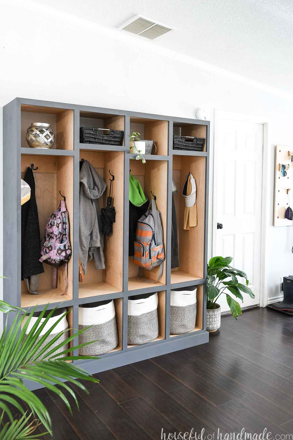 DIY mudroom storage lockers with a natural wood finish inside and gray-blue painted exteriors in an entryway filled with coats and backpacks.