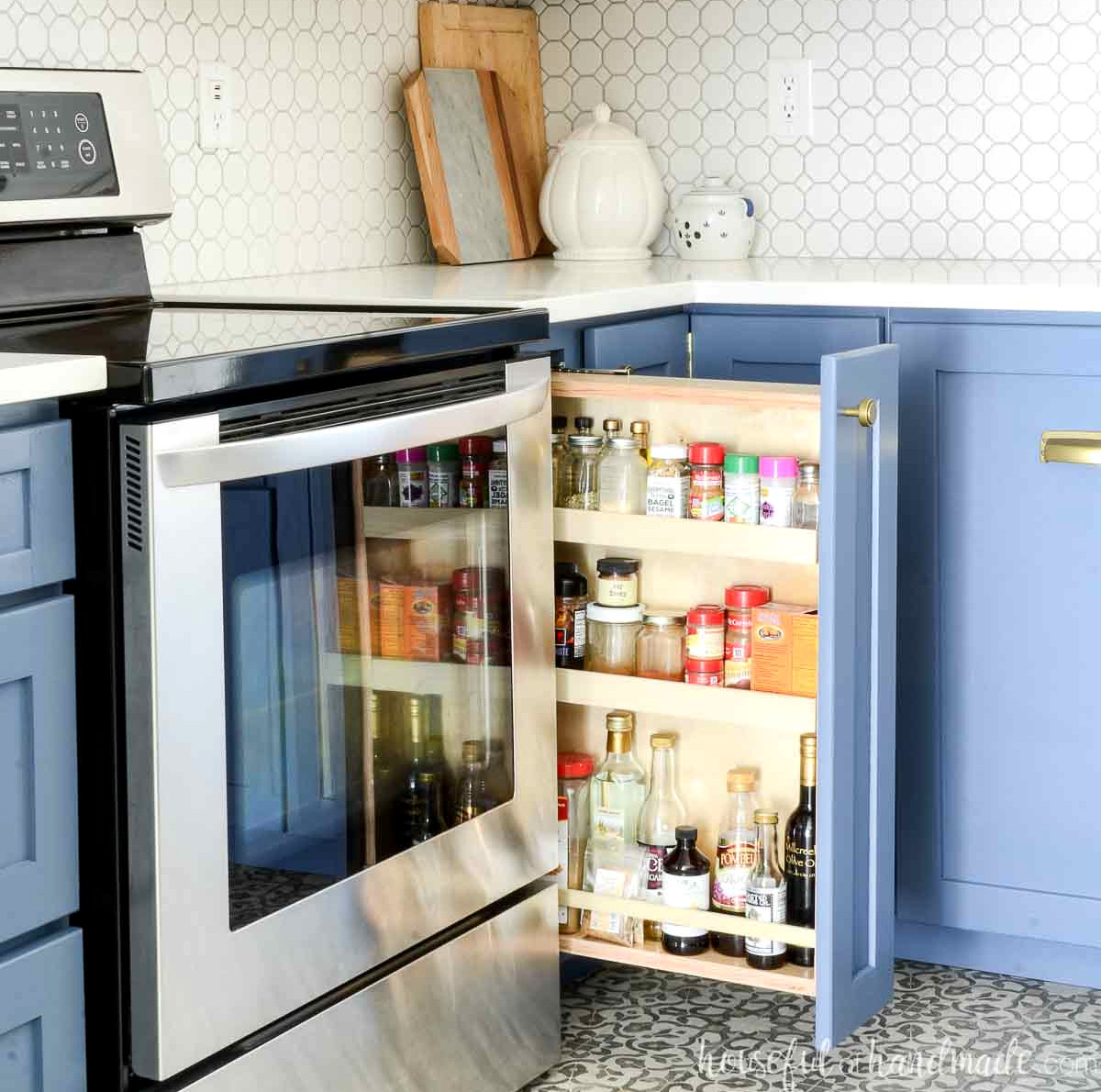 Homemade pull-out spice rack cabinet with three shelves inside a kitchen featuring blue cabinets.
