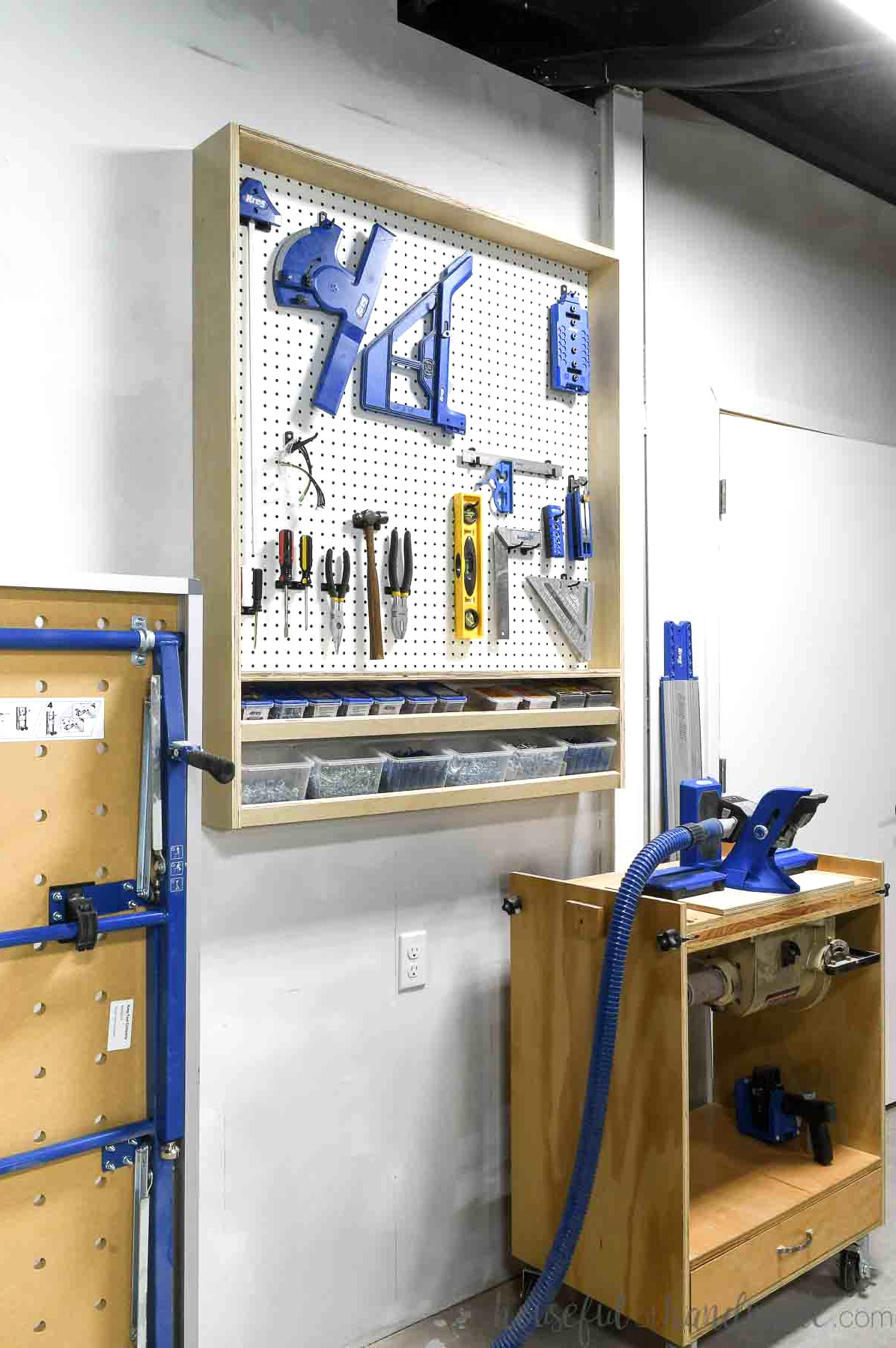 Wall-mounted pegboard cabinet in a garage, holding tools with additional larger tools positioned beside it.
