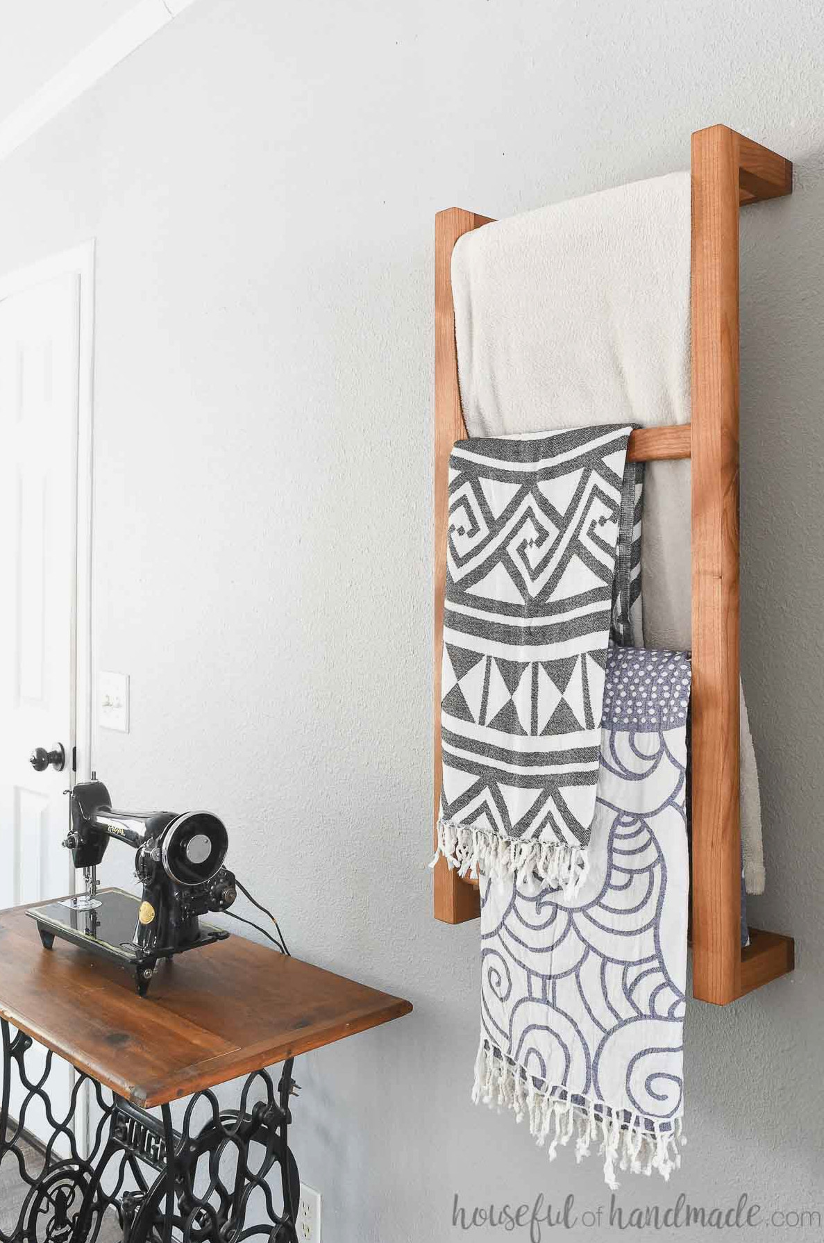 Side view of a wall-mounted ladder positioned beside a vintage sewing table with blankets draped over it.