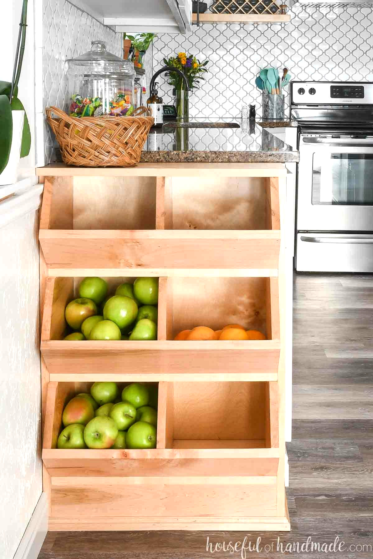 Divided wooden produce bins filled with apples and oranges, with a basket resting on top.