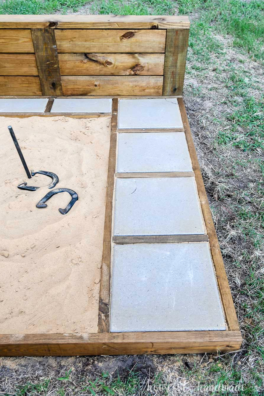 View of the right side of an ultimate DIY horseshoe pit finished in walnut stain with gray pavers.