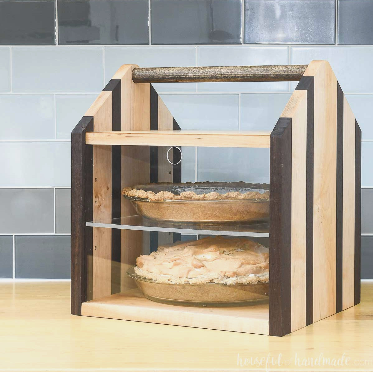 Wooden pie carrier holding two pies, featuring a dowel handle and acrylic front panel.
