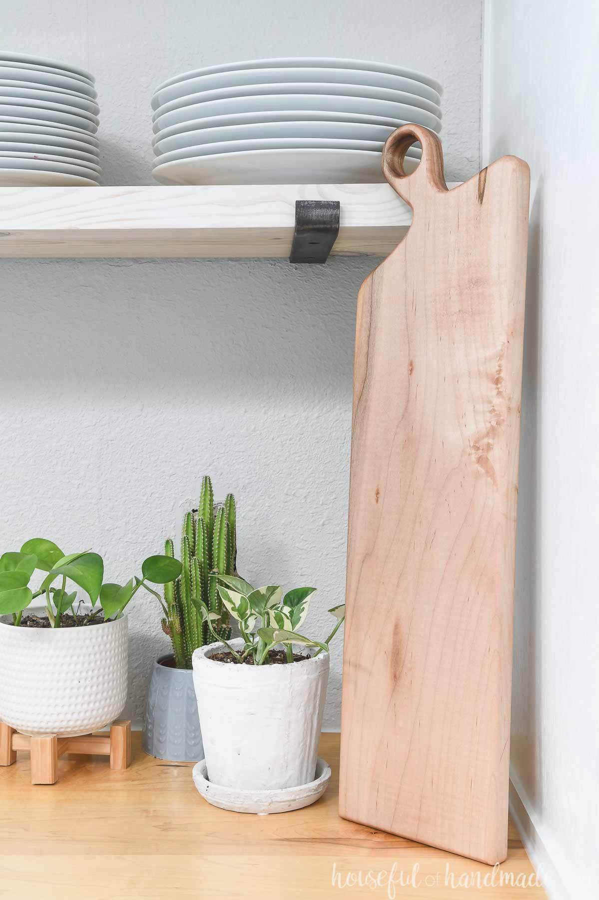 Long maple DIY breadboard resting against a cabinet and open shelving.