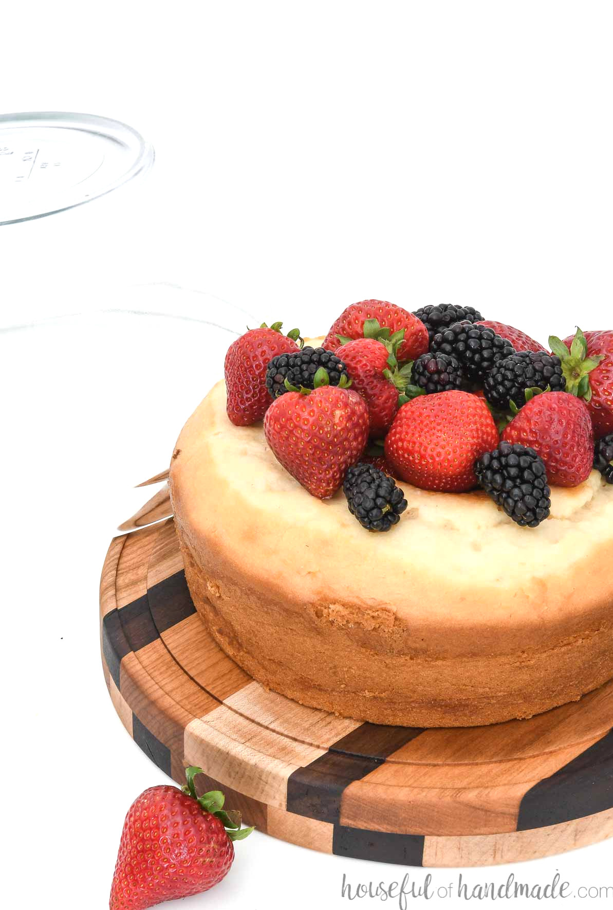 DIY wooden cake stand with a glass dome placed beside it, covering a berry-topped cake.