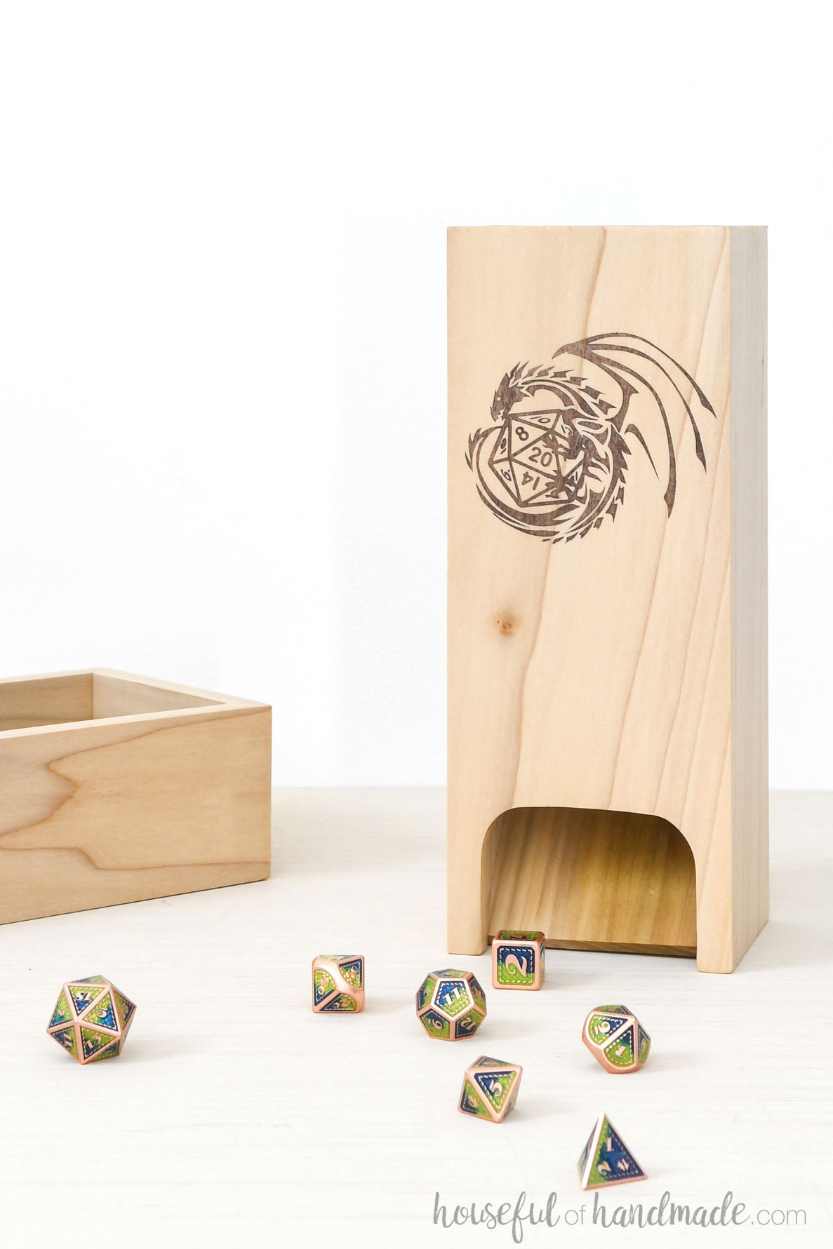 Wooden dice tower with a dragon and dice motif on the front beside a matching tray and scattered dice.