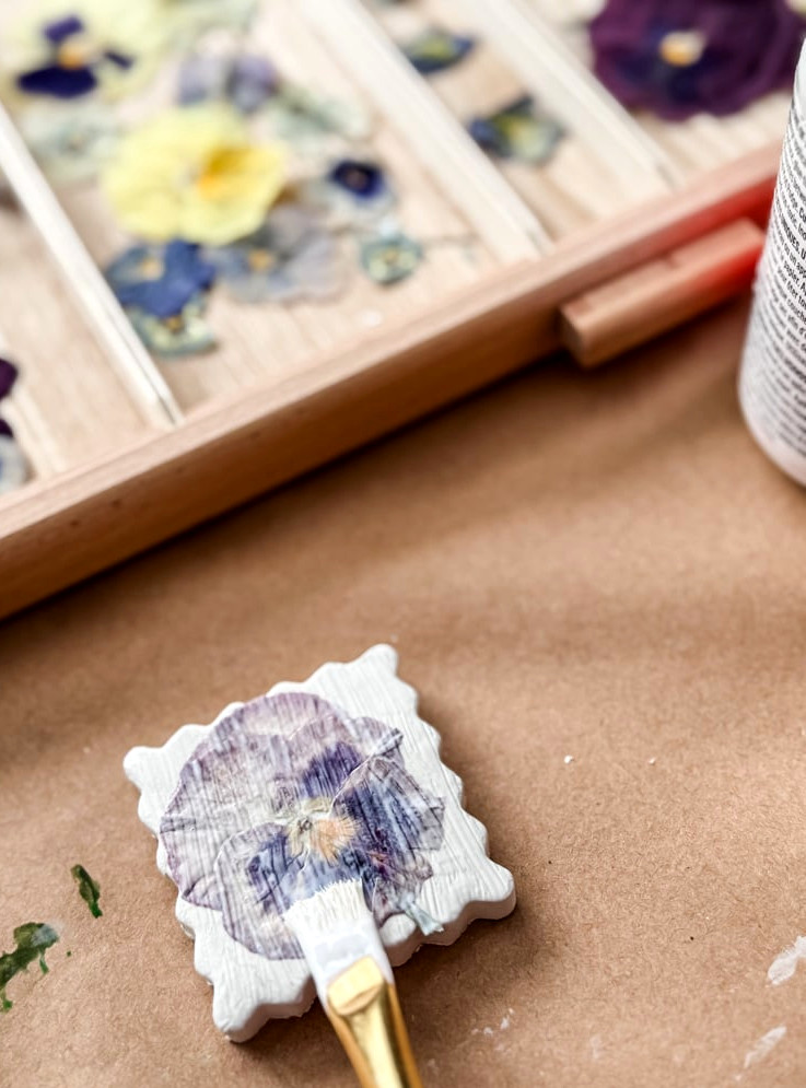 Mod Podge coating a pressed pansy on a clay piece