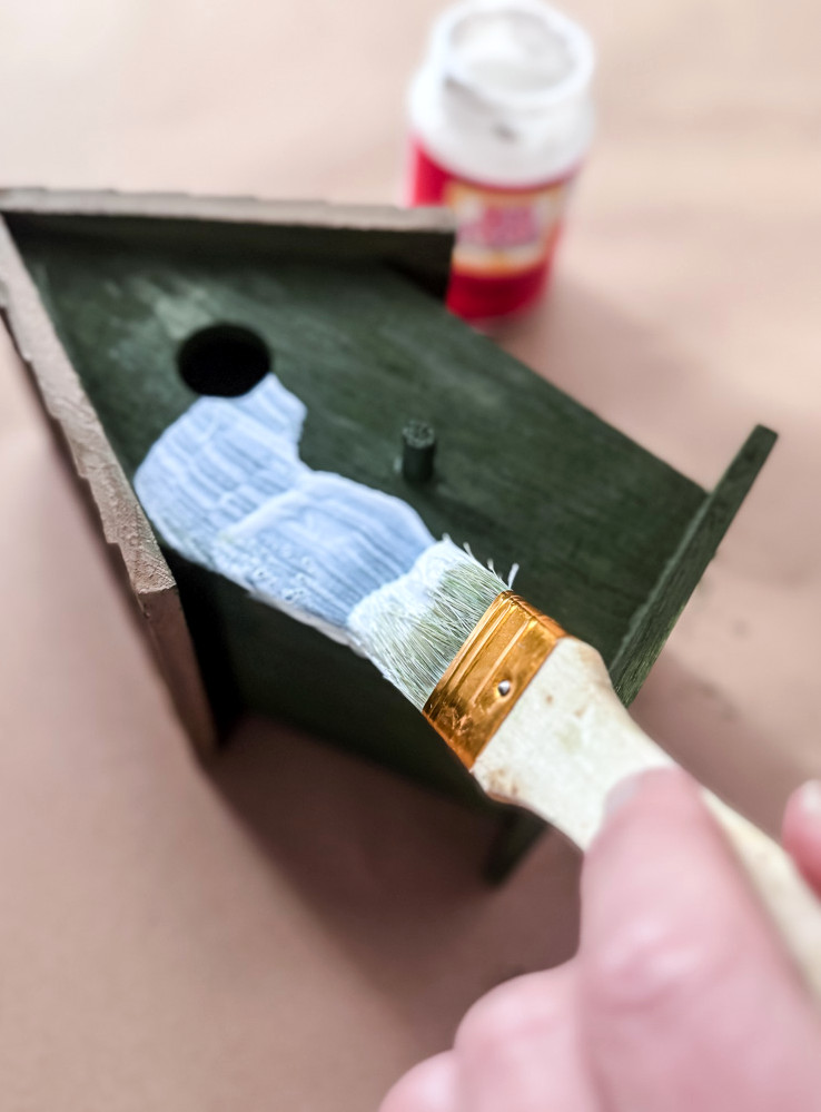 applying mod podge to a wooden birdhouse