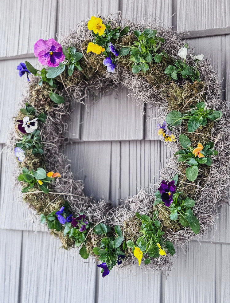 live pansy wreath hanging on a grey shingled house