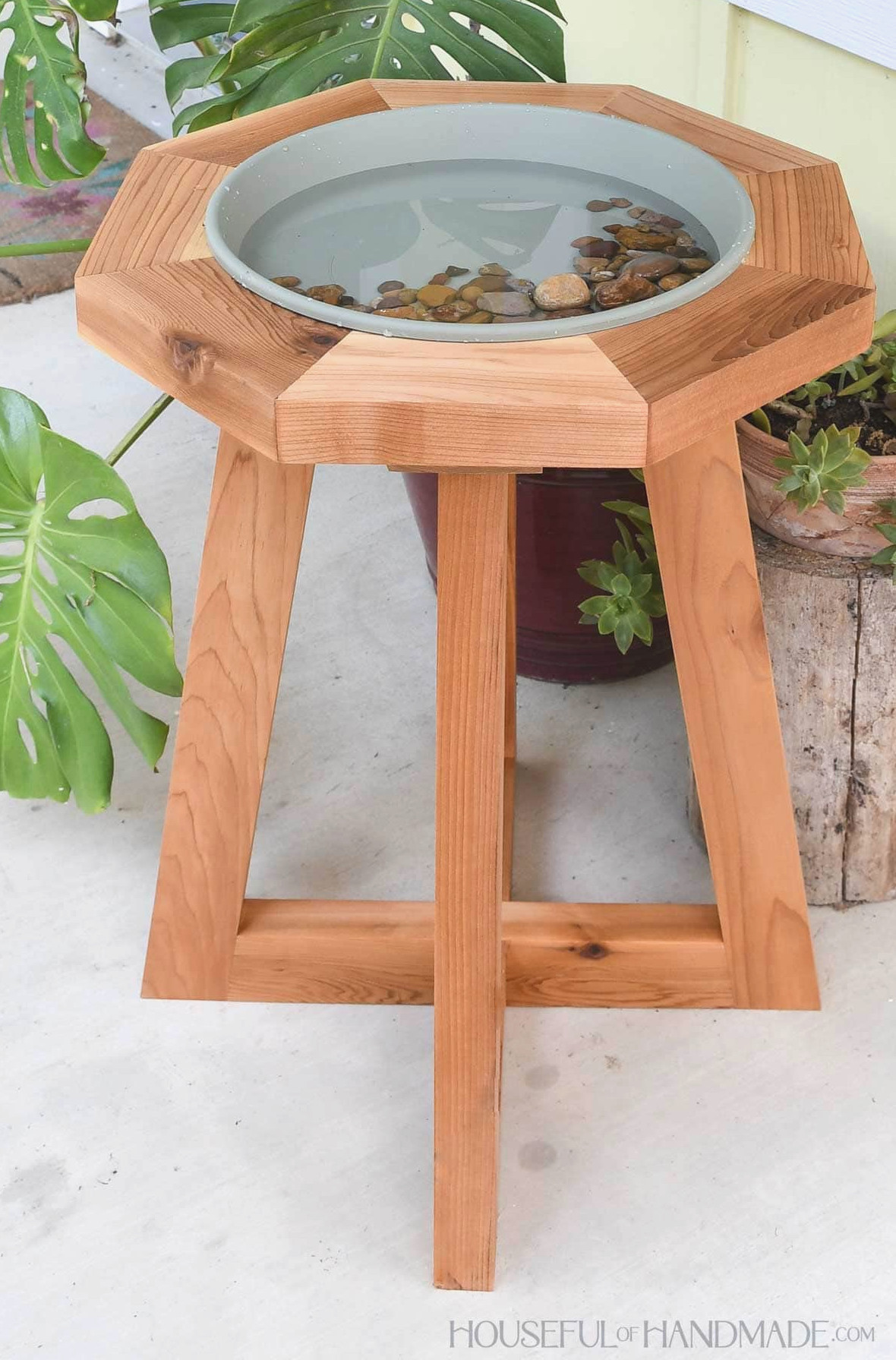 Large cedar wooden birdbath with a sage green saucer filled with water and rocks on top.
