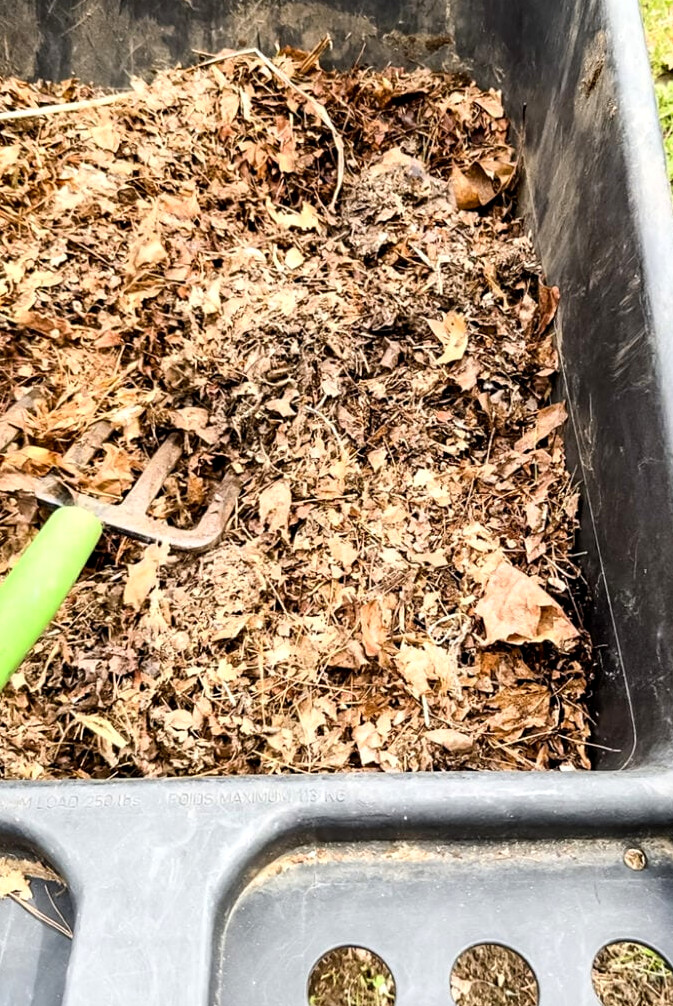 using a pitch fork to scoop out leaves from a gardening cart